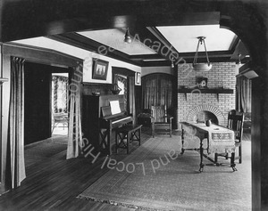 Image of View of living room with piano and table in center and fireplace at the far end